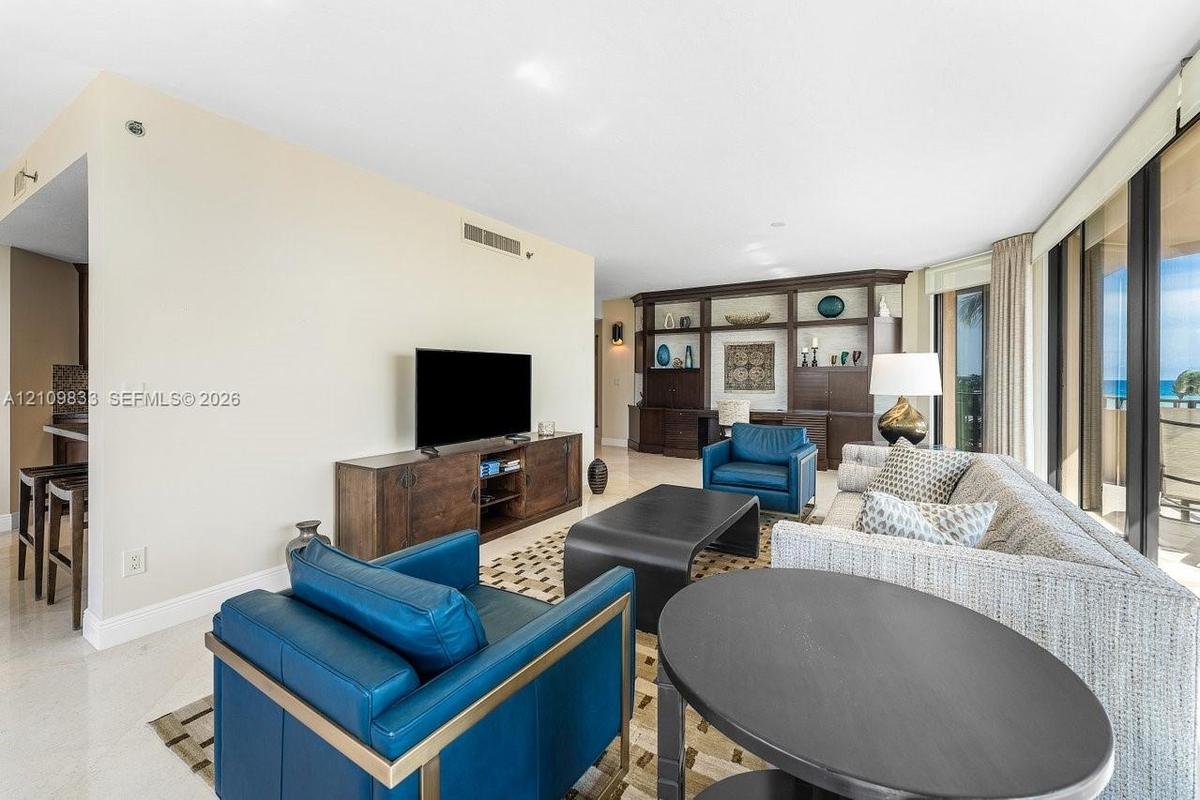 Open-concept interior featuring large-format stone flooring, floor-to-ceiling glass panel windows, and custom built-in dark wood shelving with integra
