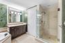 Dark wood cabinetry with stone-finish vanity top, glass-enclosed shower with tile surround, large-format tile flooring, and integrated soaking tub