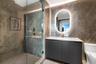 Bathroom featuring floor-to-ceiling stone tile, a glass-enclosed shower, a modern dark-finish vanity, and a backlit oval vanity mirror