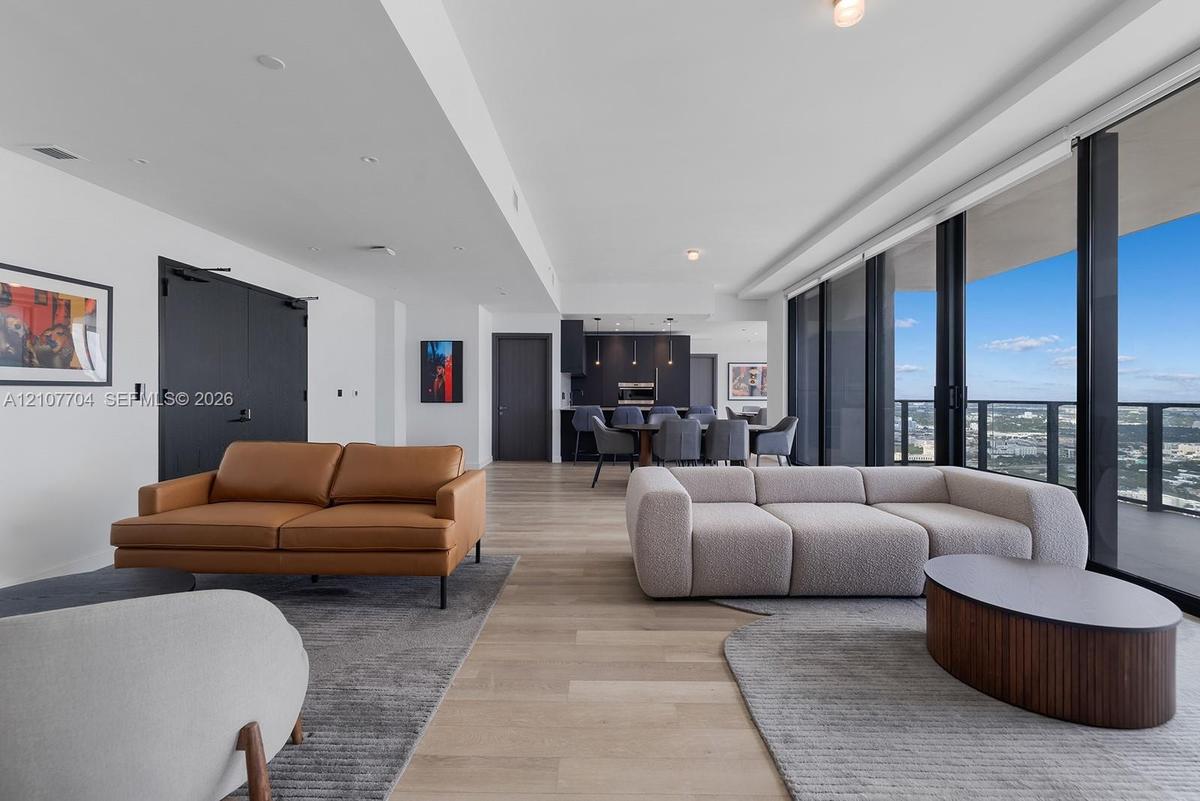 Open-concept living space featuring wood-finish flooring, floor-to-ceiling glass wall, recessed lighting, and kitchen cabinetry with integrated applia