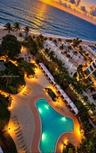 Aerial perspective of coastal property featuring an expansive swimming pool with hardscaped surround, multiple cabanas, mature palm trees, and direct 
