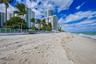 Sandy beach shoreline featuring direct coastal access, glass-panel perimeter fencing, and mature palm trees