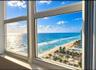 Floor-to-ceiling windows with white frames, showcasing coastal scenery including an expansive ocean and sand shoreline