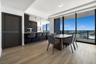 Open-concept interior featuring light wood-finish flooring, floor-to-ceiling windows, matte black cabinetry, built-in stainless steel appliances, and 
