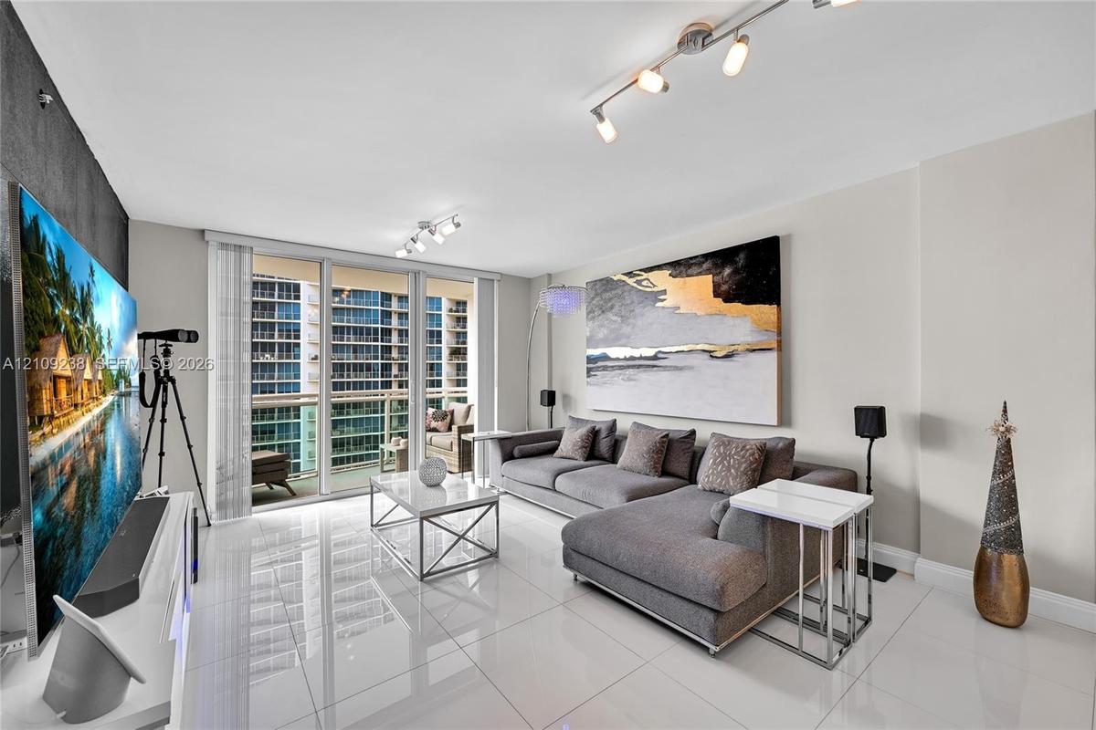 Large-format tile flooring, floor-to-ceiling glass sliding doors, private balcony, and multi-directional track lighting