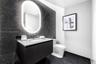Floating vanity with a light-toned countertop, dark stone-finish wall tile, integrated oval back-lit mirror, and modern wall-mounted faucet