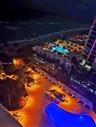 Aerial perspective of oceanfront property featuring a multi-level swimming pool, expansive paved terrace, linear cabanas, and manicured grounds