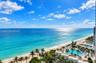 High-altitude perspective featuring an expansive ocean horizon, sandy coastline, and a multi-pool aquatic complex with surrounding palm trees