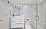 Bathroom featuring a white three-drawer vanity, illuminated rectangular mirror, one-piece elongated toilet, and a glass-enclosed shower with polished 