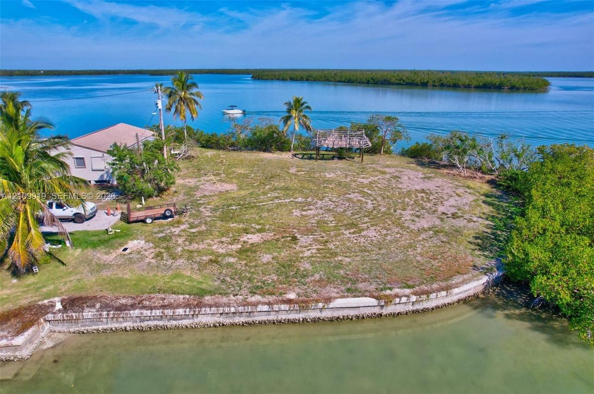 Waterfront lot featuring a concrete seawall, expansive grounds, and a thatched-roof pavilion