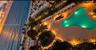Aerial perspective of beachfront property featuring an expansive swimming pool, stone-paved pool deck, palm tree landscaping, and direct access to the