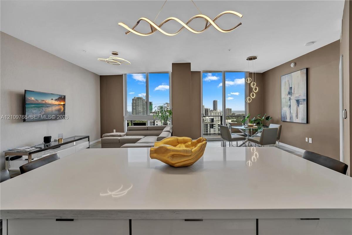 Expansive quartz island with white cabinetry, floor-to-ceiling windows, and contemporary sculptural lighting fixtures