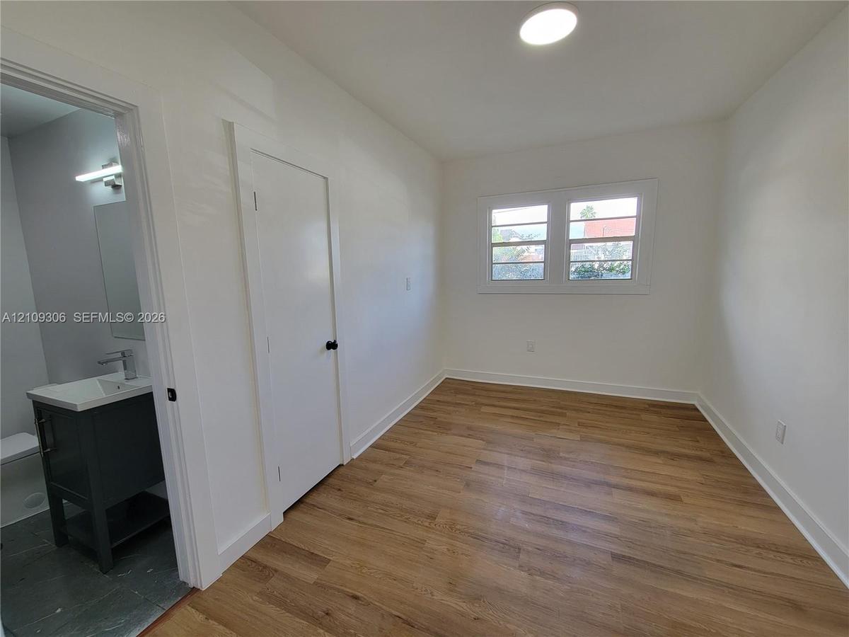 Interior space featuring wood-finish flooring, white walls, dual-pane windows, and a recessed ceiling light, accompanied by a bathroom with a charcoal