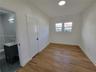 Interior space featuring wood-finish flooring, white walls, dual-pane windows, and a recessed ceiling light, accompanied by a bathroom with a charcoal
