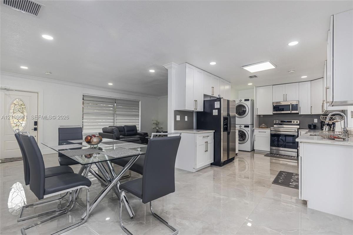 Kitchen featuring white shaker-style cabinetry, stainless steel appliances, stacked laundry unit, polished tile flooring, and recessed lighting