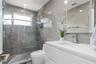 Bathroom featuring a glass-enclosed walk-in shower with floor-to-ceiling stone-finish tile, a floating white vanity with a rectangular sink, and a bui