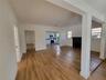 Open living space featuring wood-finish flooring, a painted brick fireplace, and kitchen cabinetry with integrated stainless steel appliances