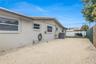 Exterior side profile featuring a light-toned stucco finish, horizontal sliding windows, gravel ground cover, and a privacy fence