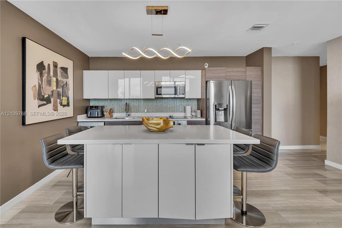 Kitchen featuring a central island with a quartz countertop, high-gloss white cabinetry, stainless steel appliances, a geometric LED pendant light, an