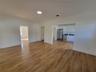 Open-concept interior featuring wood-finish flooring, white flat-panel cabinetry, stainless steel kitchen appliances, and recessed lighting