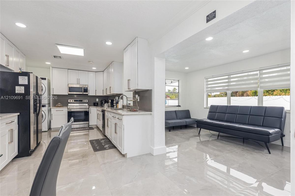 Kitchen featuring white shaker cabinetry, stone-finish countertops, stainless steel appliances, and large-format tile flooring