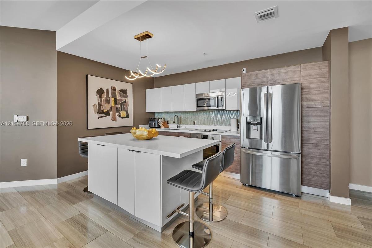 Kitchen featuring wood-finish cabinetry, a central island with a stone-composite countertop, stainless steel appliances, and wood-finish flooring