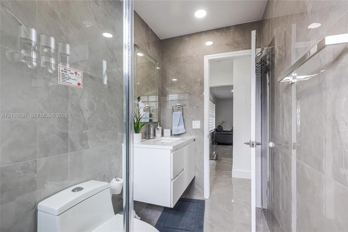 Full-height stone-finish wall tile, floating white vanity, recessed ceiling lighting, glass-enclosed shower, and polished stone-finish flooring