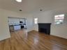 Wood-finish flooring, matte black fireplace surround, white flat-panel cabinetry, stainless steel kitchen appliances, and windows with white casings