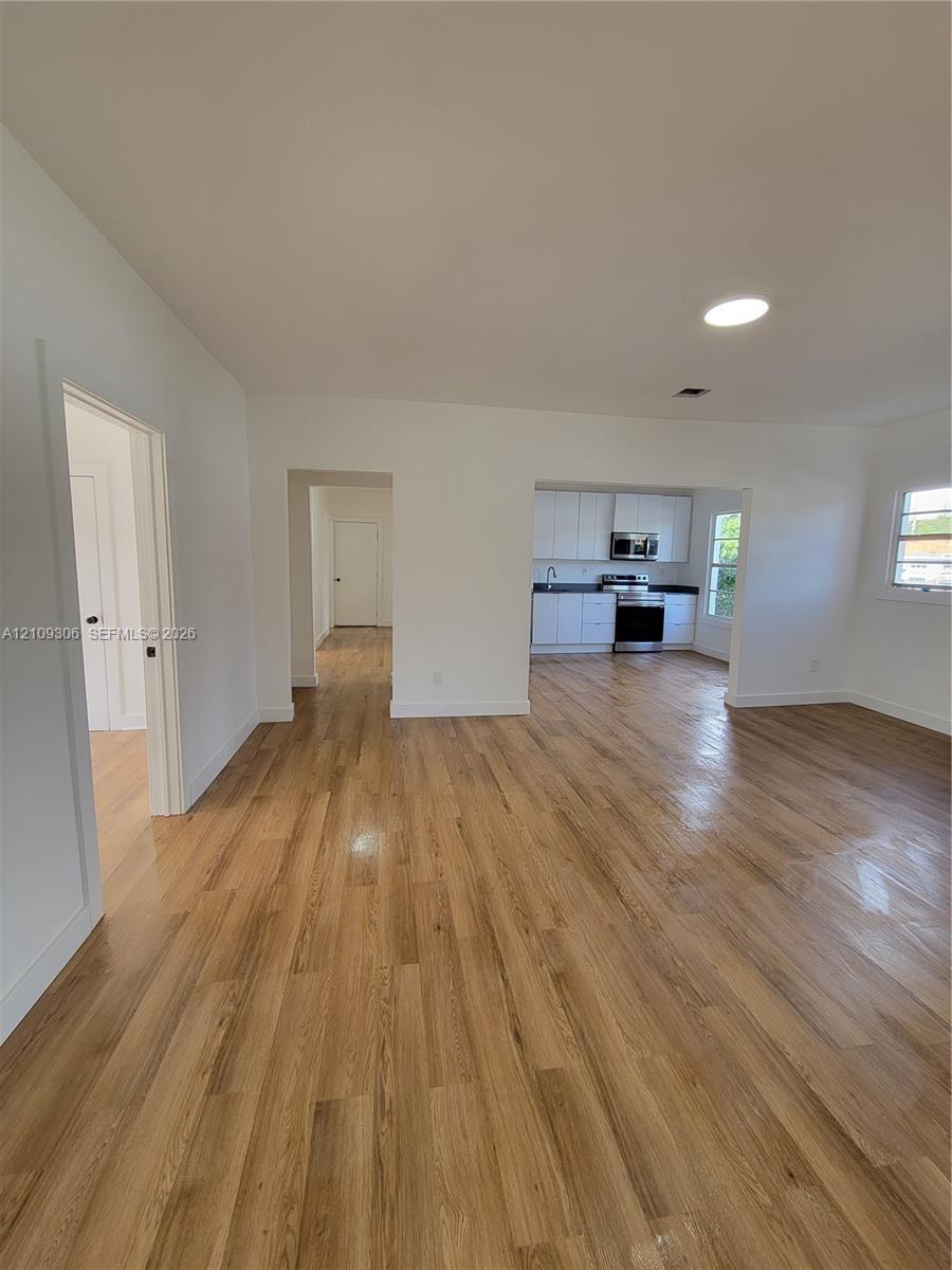 Open-concept interior featuring light wood-finish flooring, recessed lighting, and kitchen cabinetry with integrated stainless steel appliances