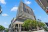 High-rise building featuring a glass facade, multiple cantilevered balconies, decorative geometric screening, and ground-level storefronts with floor-
