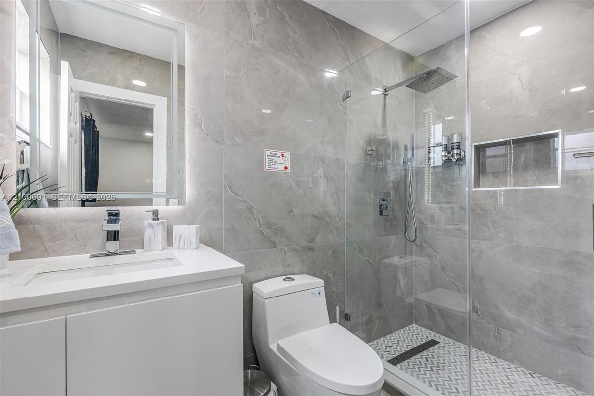 Bathroom featuring large-format gray tile wall surrounds, a frameless glass shower enclosure with a rainfall showerhead, a built-in tiled shower niche