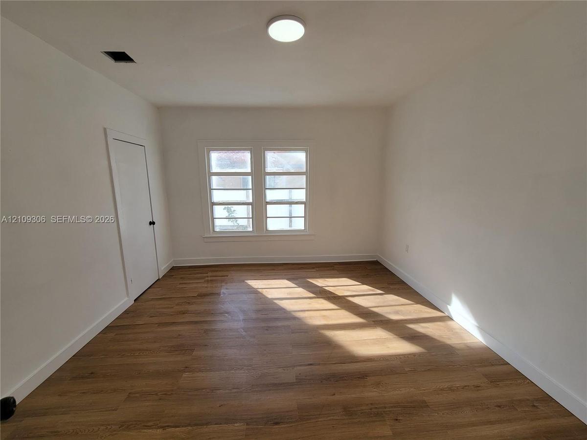 Interior room featuring wood-finish flooring, white walls, double-pane windows with horizontal muntins, and a flush-mount ceiling light fixture