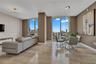 Open-concept interior featuring floor-to-ceiling windows, neutral wall tones, polished stone flooring, modern geometric chandelier lighting, and a pri