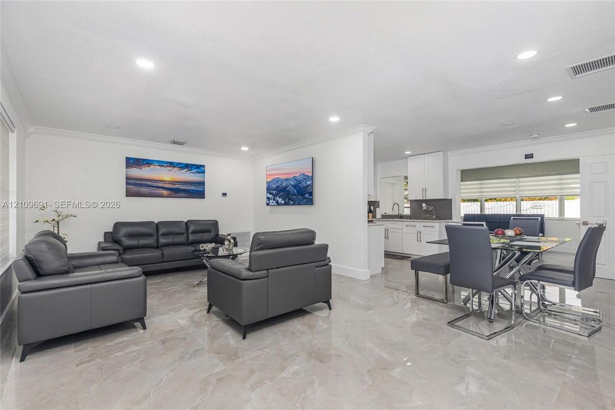 Open-concept interior featuring large-format polished tile flooring, recessed lighting, crown molding, and white shaker-style cabinetry