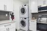 Stacked laundry unit featuring white cabinetry, stone-finish countertops, stainless steel appliances, and dark gray backsplashes
