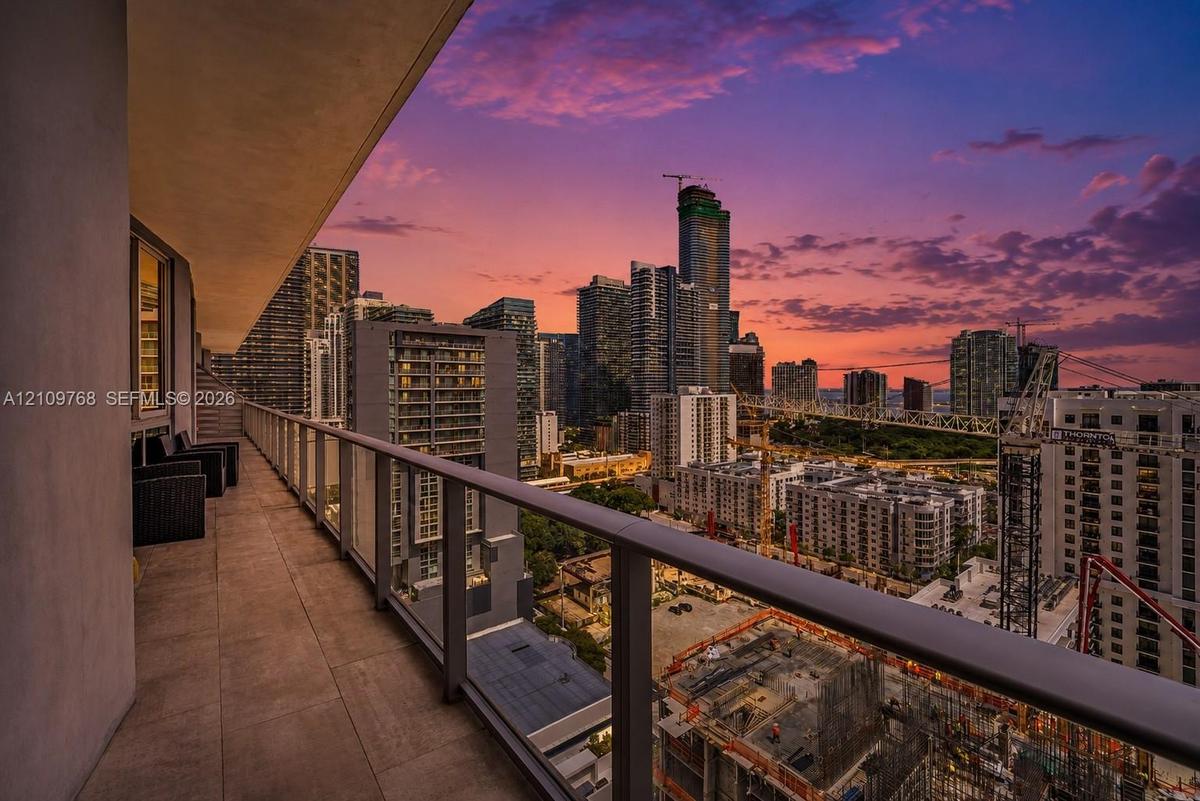 Covered balcony featuring tile flooring and a glass-paneled railing overlooking an urban cityscape
