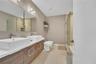 Dual-sink vanity with wood-finish cabinetry, rectangular vessel sinks, large wall-to-wall mirror, glass-enclosed shower, and tile flooring