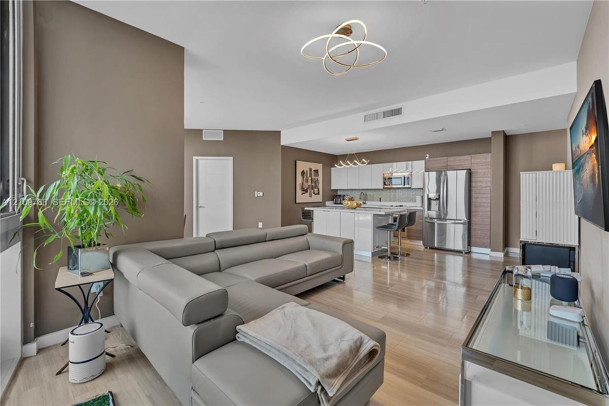Open-concept living space featuring high-gloss cabinetry, stainless steel appliances, wood-finish flooring, and contemporary geometric light fixtures