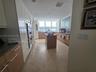 Kitchen featuring two-tone cabinetry with wood-finish lower units and high-gloss upper cabinetry, stone countertops, a central kitchen island, and lar