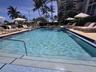Rectangular swimming pool featuring tiled steps, metal handrails, a paved deck, and mature palm trees