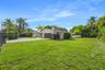Single-story exterior featuring a light-toned facade, multi-car garage, expansive lawn, mature palm trees, and perimeter fencing