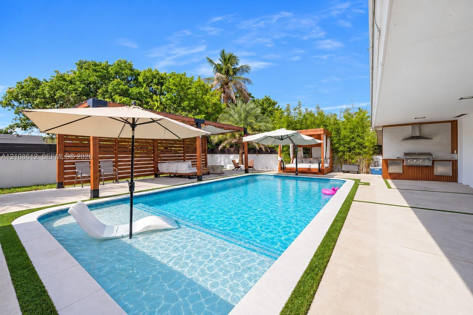 Outdoor living space featuring a swimming pool with a sun shelf, paved patio with integrated artificial turf, wood-slat pergola, and a built-in outdoo