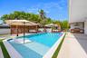Outdoor living space featuring a swimming pool with a sun shelf, paved patio with integrated artificial turf, wood-slat pergola, and a built-in outdoo