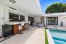 Covered outdoor patio featuring a built-in bar with vertical wood-slat detailing, concrete hardscaping, recessed lighting, and a swimming pool framed 