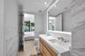 Bathroom featuring a dual-sink vanity with stone countertops, a large LED-backlit mirror, and stone wall tiling