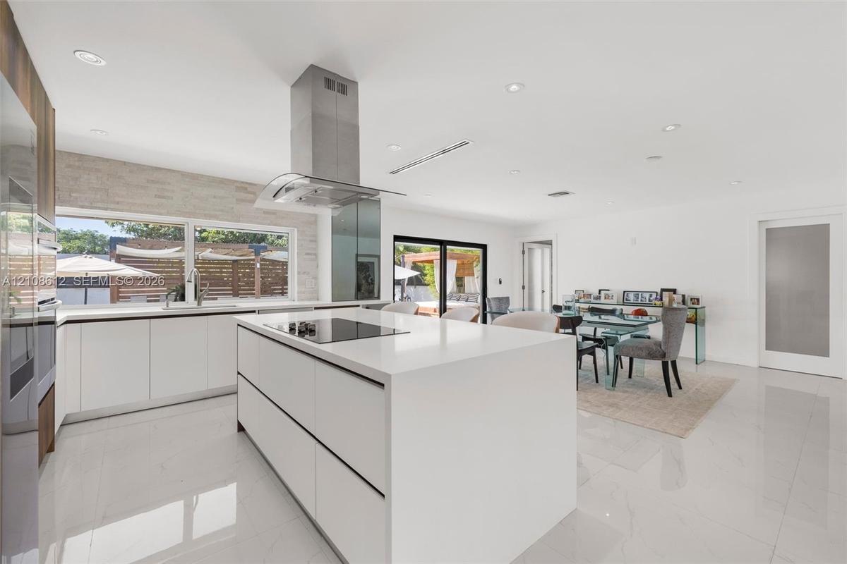 Modern kitchen featuring a central island with a solid-surface countertop and cooktop, sleek flat-panel cabinetry, a stainless steel chimney-style ran