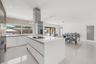 Modern kitchen featuring a central island with a solid-surface countertop and cooktop, sleek flat-panel cabinetry, a stainless steel chimney-style ran