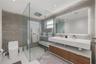Bathroom featuring a glass-enclosed walk-in shower with a rainfall showerhead, floating dual-sink vanity with wood-finish cabinetry, stone-texture wal