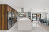 Modern kitchen featuring floor-to-ceiling wood-finish cabinetry, a white stone-surface island, stainless steel built-in appliances, recessed lighting,