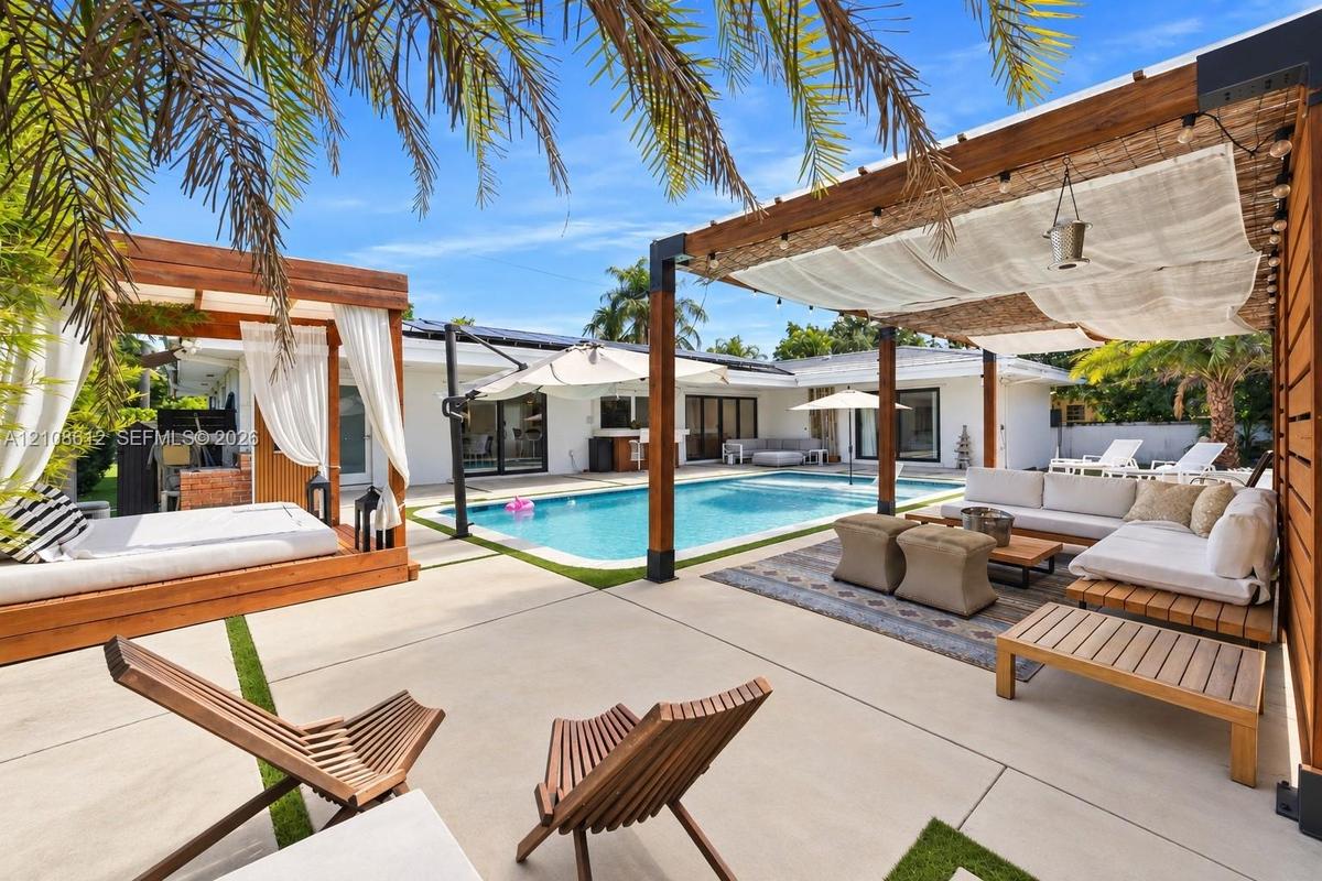 Outdoor living area featuring a custom concrete patio, rectangular swimming pool, integrated wood-beam pergolas, and built-in masonry structures
